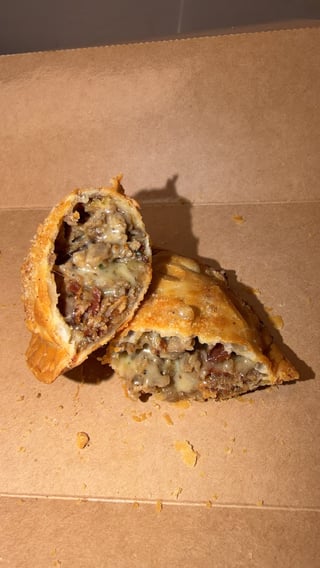 Cut empanada showing meat and vegetable filling on brown surface with crumbs
