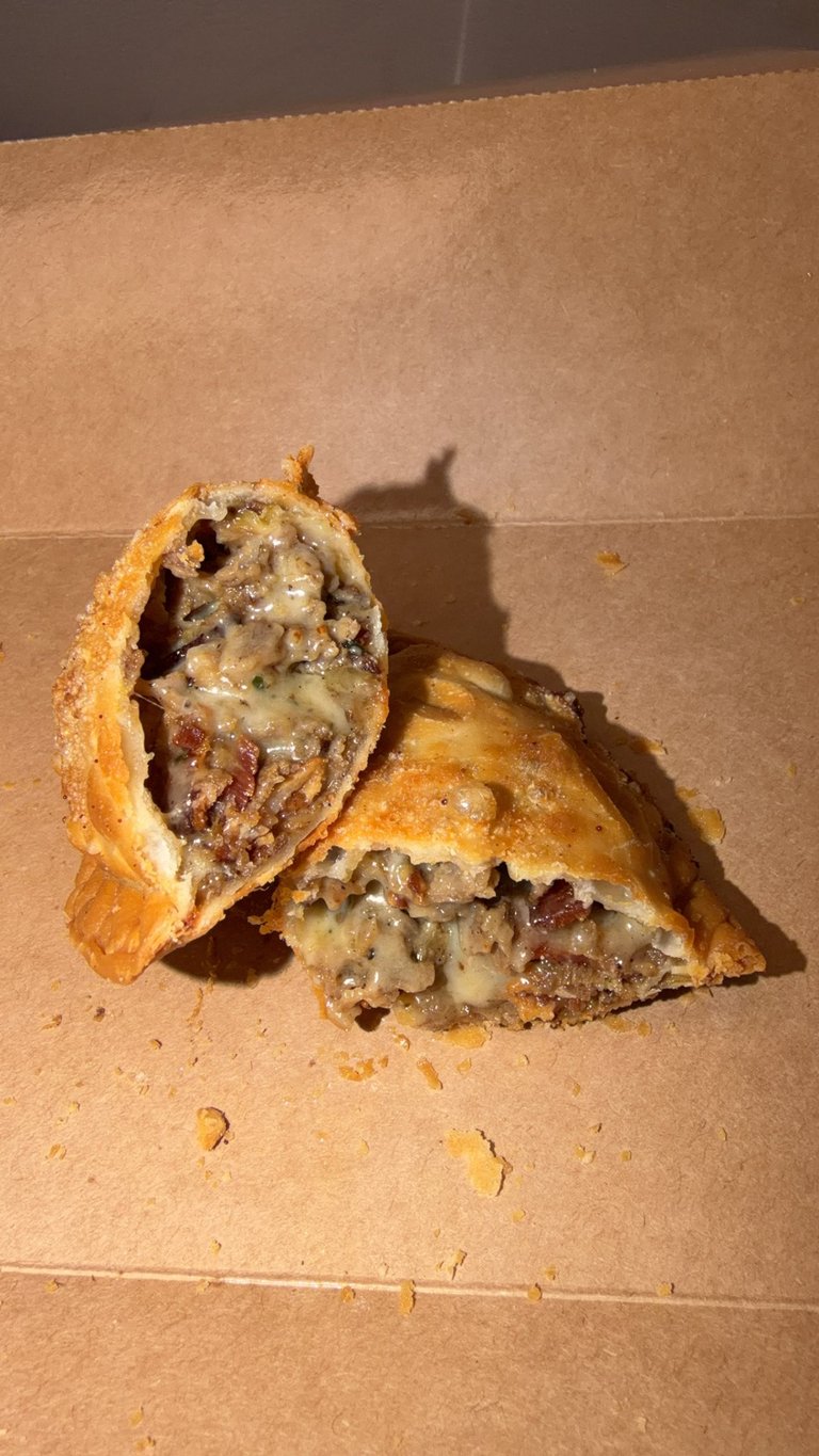 Cut empanada showing meat and vegetable filling on brown surface with crumbs